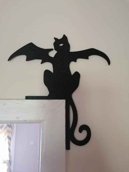 Black silhouette of a cat with bat wings perched on a door frame against a light background.
