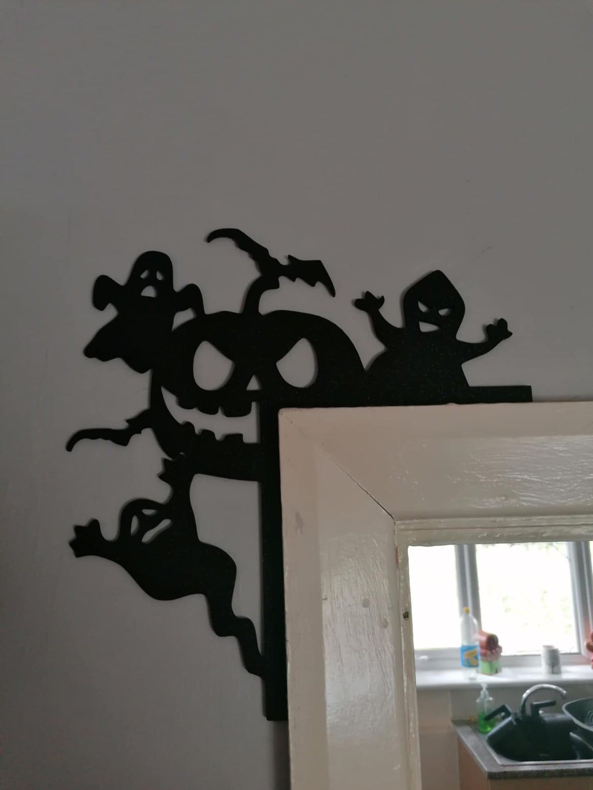 Black silhouette of a jack‑o’‑lantern surrounded by ghosts, placed on top of a door frame.