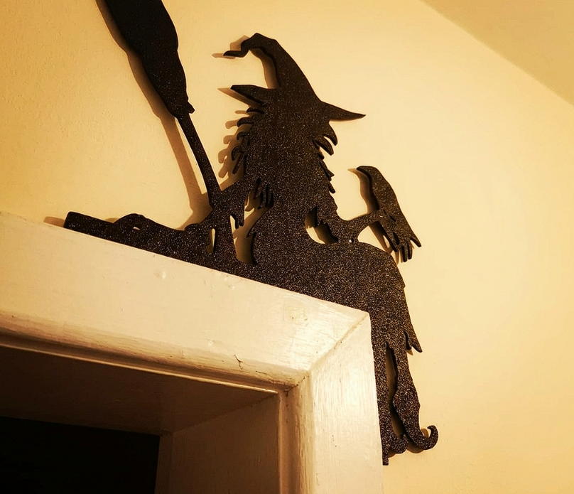 Decorative pla wall art of a witch with a broom on a white shelf against a beige wall.