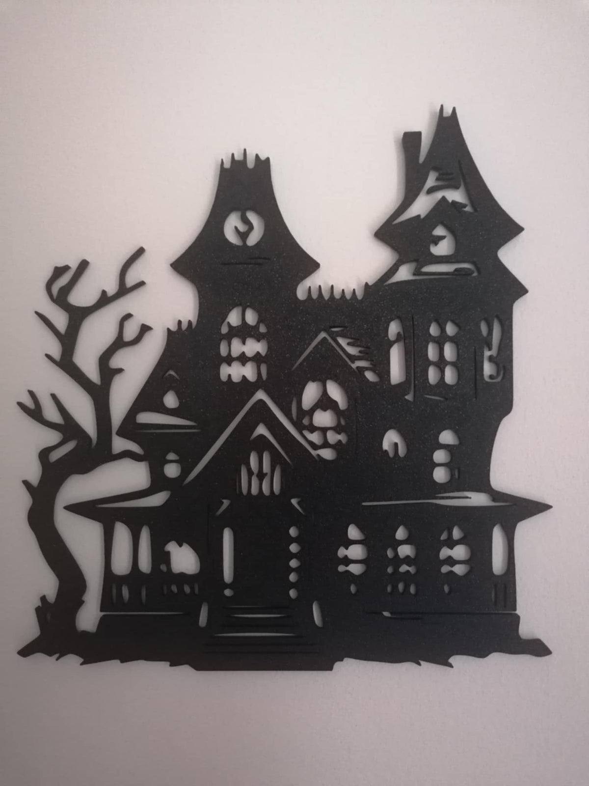 Black haunted‑house silhouette with tall gothic towers, irregular windows, and a twisted tree on the side, displayed on a white background.